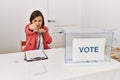 Beautiful middle age hispanic woman at political election sitting by ballot punching fist to fight, aggressive and angry attack, Royalty Free Stock Photo