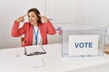 Beautiful middle age hispanic woman at political election sitting by ballot smiling pointing to head with both hands finger, great