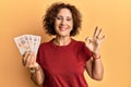 Beautiful middle age mature woman holding 10 united kingdom pounds banknotes doing ok sign with fingers, smiling friendly