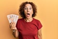 Beautiful middle age mature woman holding 10 united kingdom pounds banknotes scared and amazed with open mouth for surprise,