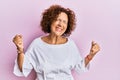 Beautiful middle age mature woman wearing elegant clothes over pink background very happy and excited doing winner gesture with Royalty Free Stock Photo