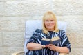 Beautiful middle age smiling scandinavian woman in outdoor patio reading book sitting in armchair.