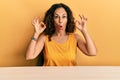 Beautiful middle age woman wearing casual clothes sitting on the table looking surprised and shocked doing ok approval symbol with Royalty Free Stock Photo