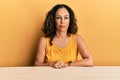 Beautiful middle age woman wearing casual clothes sitting on the table relaxed with serious expression on face Royalty Free Stock Photo