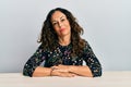 Beautiful middle age woman wearing casual clothes sitting on the table relaxed with serious expression on face Royalty Free Stock Photo