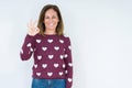 Beautiful middle age woman wearing heart sweater over isolated background smiling positive doing ok sign with hand and fingers