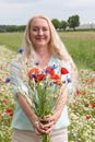 beautiful middle-aged blonde woman stands among a flowering field of poppies Royalty Free Stock Photo