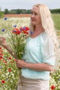 beautiful middle-aged blonde woman stands among a flowering field of poppies Royalty Free Stock Photo