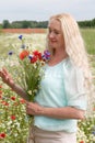 beautiful middle-aged blonde woman stands among a flowering field of poppies Royalty Free Stock Photo