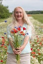 beautiful middle-aged blonde woman stands among a flowering field of poppies Royalty Free Stock Photo