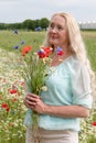 beautiful middle-aged blonde woman stands among a flowering field of poppies Royalty Free Stock Photo