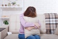 Beautiful middle aged brunette woman holding a pillow and crying on sofa. Home background, interior. Menopause time. Copy space Royalty Free Stock Photo