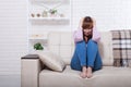 Sad middle aged woman sitting on sofa with clamped knees and crying. Home background Royalty Free Stock Photo