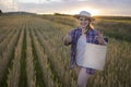 A beautiful middle-aged farmer woman in a straw hat and a plaid shirt stands in a field of golden ripening wheat during the daytim