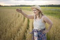 A beautiful middle-aged farmer woman in a straw hat and a plaid shirt stands in a field of golden ripening wheat during the daytim