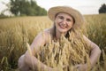 A beautiful middle-aged farmer woman in a straw hat and a plaid shirt stands in a field of golden ripening wheat during the daytim