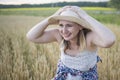 A beautiful middle-aged farmer woman in a straw hat and a plaid shirt stands in a field of golden ripening wheat during the daytim