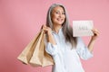 Beautiful middle aged lady holds paper shopping bags and card with word Sale in studio