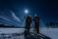 Beautiful middle aged men and women in snowshoes stand in night rare snowy winter forest under full moon light. Night walk Lapland Royalty Free Stock Photo