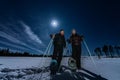 Beautiful middle aged men and women in snowshoes stand in night rare snowy winter forest under full moon light. Night walk Lapland