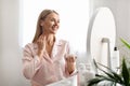 Beautiful middle aged woman applying moisturizing cream on her neck at home Royalty Free Stock Photo