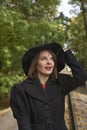 Beautiful middle-aged woman in black coat and wide-brimmed hat looks up admiringly.Woman in retro style. Vertical frame