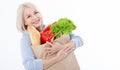 Beautiful middle-aged woman with blond hair holds products from the store in paper bag. Bread, herbs, pepper, green lettuce in her Royalty Free Stock Photo