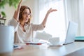 Beautiful middle-aged woman in glasses extremely surprised with new higher taxes watching, throwing bills at laptop in home office Royalty Free Stock Photo