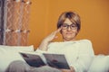 Beautiful middle aged woman in glasses reading book and enjoy while sitting on couch Royalty Free Stock Photo