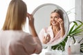 Beautiful Middle Aged Woman Looking In Mirror And Applying Moisturising Eye Cream Royalty Free Stock Photo