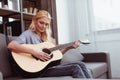 beautiful middle aged woman playing guitar while sitting on sofa Royalty Free Stock Photo