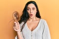 Beautiful middle eastern woman holding comb loosing hair scared and amazed with open mouth for surprise, disbelief face Royalty Free Stock Photo