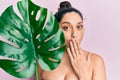 Beautiful middle eastern woman holding green plant leaf close to face covering mouth with hand, shocked and afraid for mistake Royalty Free Stock Photo