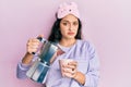 Beautiful middle eastern woman wearing sleep mask and pyjama drinking coffee clueless and confused expression