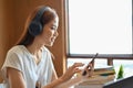 Asian female university student listening to music with headphones and using smartphone Royalty Free Stock Photo