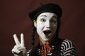 Beautiful mime girl grimaces and shows a victory sign with her hand