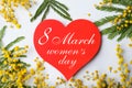 Beautiful mimosa flowers and heart shaped greeting card with text 8 March Women`s Day on grey background, flat lay Royalty Free Stock Photo