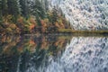 Beautiful mixed autumn and winter scene with reflection in the mirror lake.