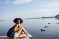 Beautiful mixed race female teenager sits on wooden pier and drinks cocktail in plactic glass