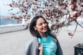 Beautiful model in blue dress and grey coat by spring blooming tree