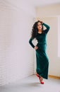 Beautiful model in emerald velvet dress standing near white brick wall