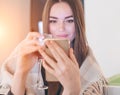 Beautiful model fashion girl drinking red wine at home, looking at her smartphone and smiling. Beauty woman covered with plaid Royalty Free Stock Photo