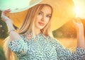 Beautiful model girl posing on a field, enjoying nature outdoors in wide brimmed straw hat. Beauty blonde young woman