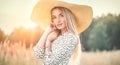 Beautiful model girl posing on a field, enjoying nature outdoors in wide brimmed straw hat. Beauty blonde young woman Royalty Free Stock Photo