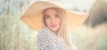 Beautiful model girl posing on a field, enjoying nature outdoors in wide brimmed straw hat. Beauty blonde young woman