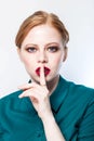 Beautiful model girl with redhead hair. Red lips. Woman holds a finger on her mouth a secret Royalty Free Stock Photo