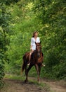 Beautiful model girl rides with horse in woods road in evening down Royalty Free Stock Photo