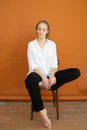 Beautiful model on orange background sitting on the chair in white shirt and black trousers