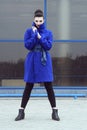 Beautiful model with perfect make up and hair scrapped back into a bun standing on the street in trendy blue coat