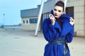 Beautiful model with perfect make up and hair scrapped back into a bun standing on the street in blue coat with leather belt Royalty Free Stock Photo